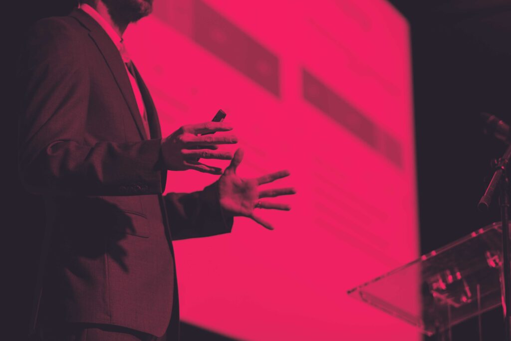 close up of a conference presenter moving his hands when talking with a presentation in the background