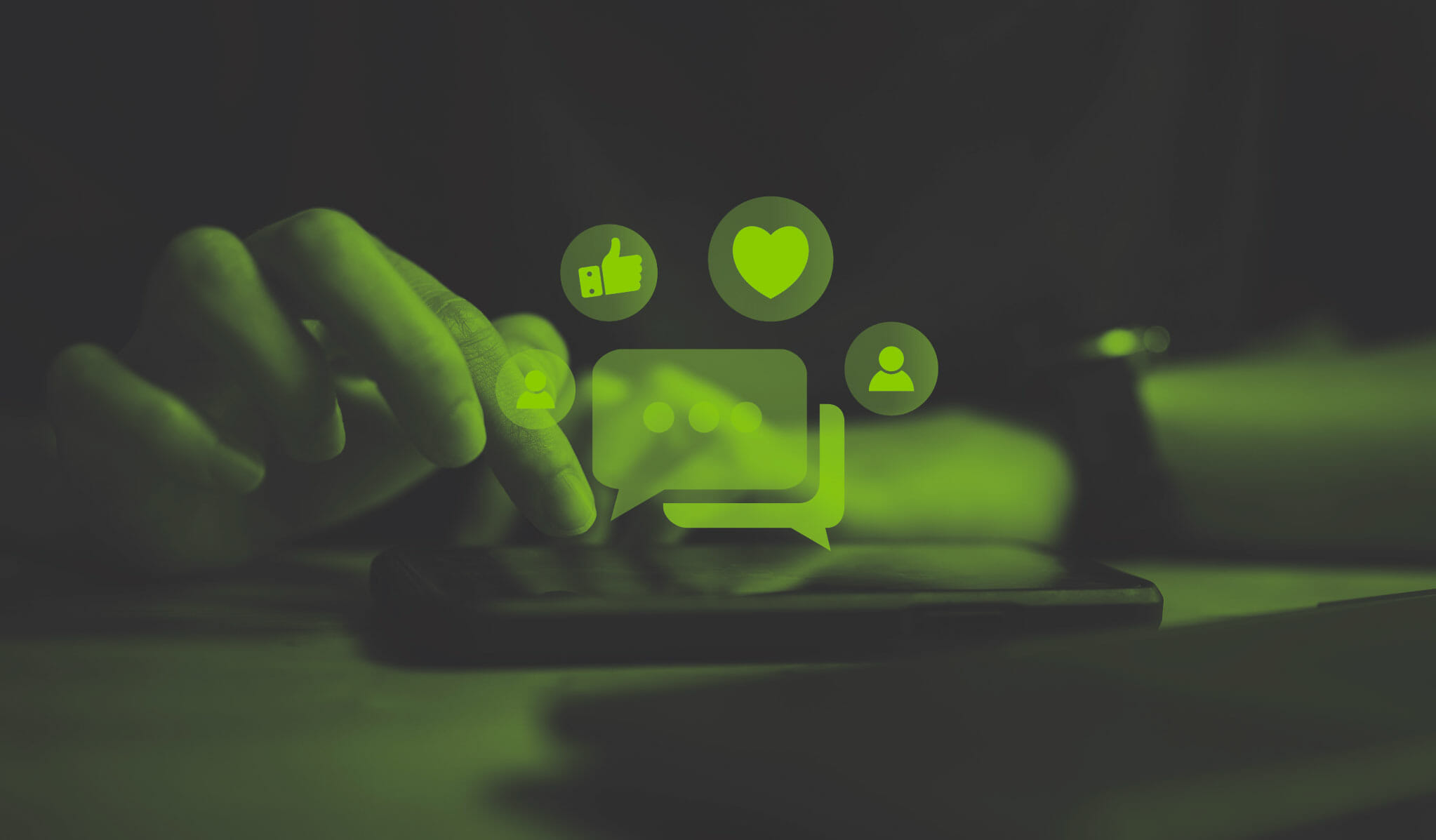 green and black image of a man's hands tapping on a phone on the table and social media icons flying above it